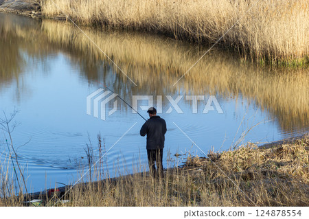 Quiet fishing at a tranquil riverbank surrounded by tall grasses during a calm afternoon 124878554