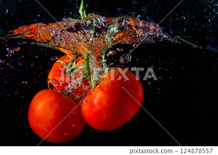 Fresh red tomato falling into water with water splash and air bubbles isolated on black background Fresh red tomato falling into water with water splash and air bubbles isolated on black background 124878557