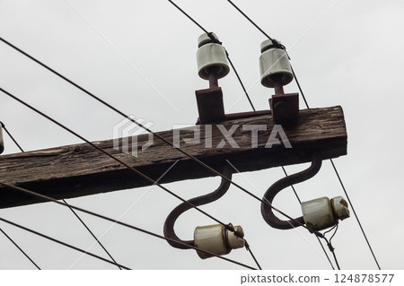 Power lines and insulators against an overcast sky in an urban area Power lines and insulators against an overcast sky in an urban area 124878577