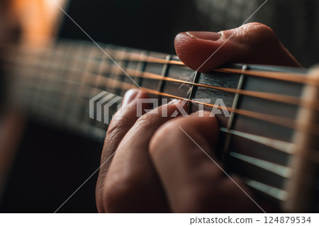 Guitar fretboard with fingers pressing strings, playing acoustic guitar 124879534