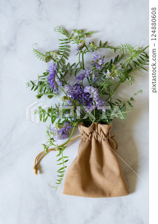 Florist at work: a pretty woman prepares a summer bouquet of white gypsophila on a gray desk. Kraft paper, scissors, greeting envelope on the table. View from above. The composition is flat. 124880608