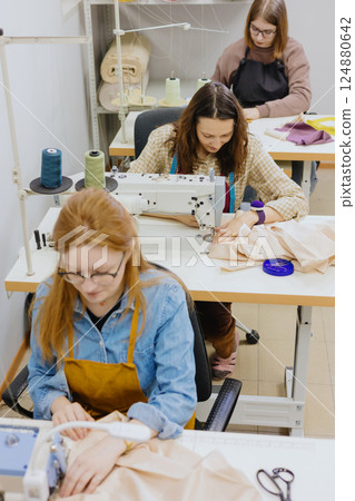 Three women seamstresses and fashion designers work in for sewing machines, clothing production. Three women seamstresses and fashion designers work in for sewing machines, clothing production. 124880642
