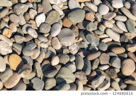 Smooth colorful pebbles scattered on a sunlit beach surface close-up shot. 124880818
