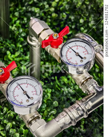 Close-up view of industrial pressure gauges connected to metal pipes amid lush greenery in a modern installation setting 124881702