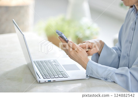 一位中年婦女在客廳一邊操作智慧型手機一邊看電腦 124882542