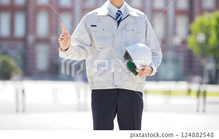 A young man in work clothes holding a helmet and pointing A young man in work clothes holding a helmet and pointing 124882548