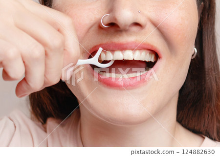 A woman uses dental floss on a stick, brushes her teeth. She is happy. The concept of healthy teeth, self-care close up photo 124882630
