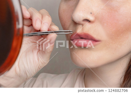 Caucasian woman looks in the mirror and pulls out her hair above her upper lip using tweezers. The girl grows a mustache. Close up photo Caucasian woman looks in the mirror and pulls out her hair above her upper lip using tweezers. The girl grows a mustache. Close up photo 124882706