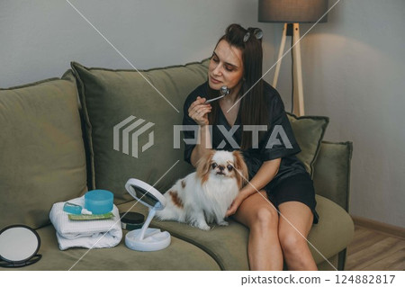 woman with facial roller, daily beauty routine, loyal pet, small dog, personal care items neatly arranged on green couch woman with facial roller, daily beauty routine, loyal pet, small dog, personal care items neatly arranged on green couch 124882817