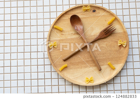 time to eat pasta. wooden plate with fork and spoon in form of clock hands. pasta on plate. 124882833