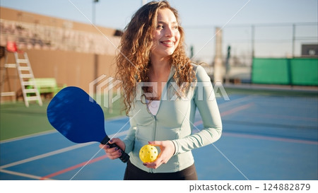Portait of a young, happy and smiling curly haired girl holding pickleball paddle 124882879