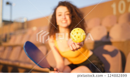 Portrait of young girl adult posing with pickleball paddle and ball on stadium chairs 124882899
