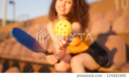 Portrait of young girl adult posing with pickleball paddle and ball on stadium chair 124882900
