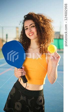 Portait of a young, happy and smiling curly haired girl holding pickleball paddle Portait of a young, happy and smiling curly haired girl holding pickleball paddle 124882908