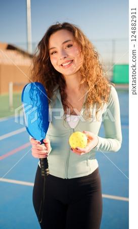 Portait of a young, happy and smiling curly haired girl holding pickleball paddle 124882911
