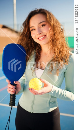 Portait of a young, happy and smiling curly haired girl holding pickleball paddle 124882912