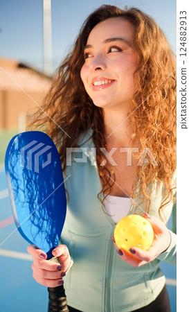 Portait of a young, happy and smiling curly haired girl holding pickleball paddle 124882913