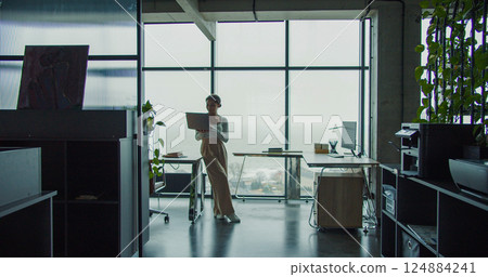 Silhouette of a young woman working on a laptop in a modern office with a large window, highlighting creativity, focus, and a serene workspace atmosphere Silhouette of a young woman working on a laptop in a modern office with a large window, highlighting creativity, focus, and a serene workspace atmosphere 124884241
