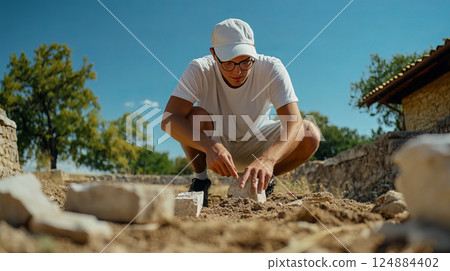 Scholar Inspecting Newly Unearthed Roman Statue in Archaeological Dig Site Under Blue Sky 124884402