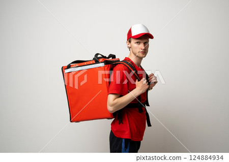 Young delivery man in a red uniform with thermal backpack. Fast food delivery service. 124884934