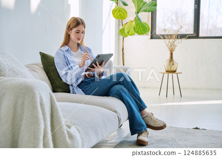 Young woman using digital tablet sitting on sofa at home 124885635