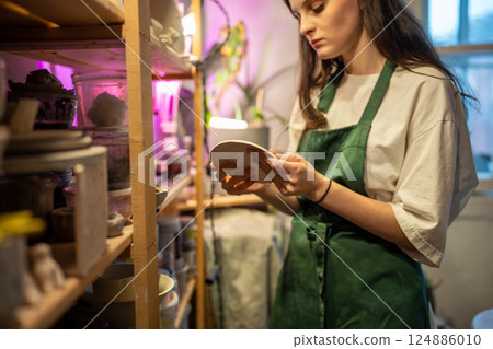Female stacking ready clay products on pottery workshop shelves for drying. Store handmade dishes 124886010