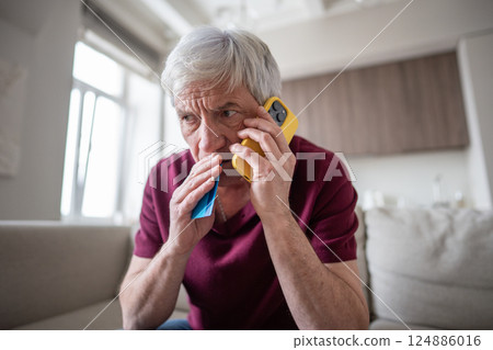 Frightened elderly man hold credit card during suspicious phone call at home, covering mouth in fear 124886016