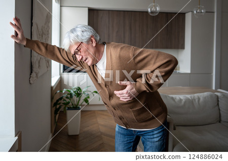 Bending suffering elderly man gasp for breath clutching chest, suspected cardiac episode at home 124886024