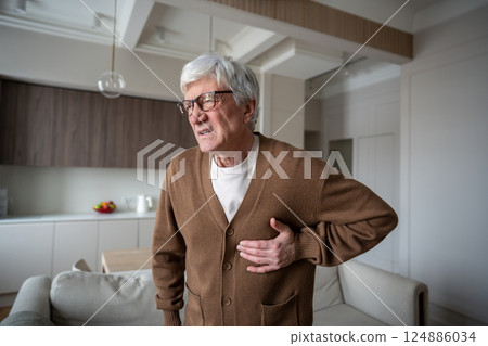 Heart attack. Suffering old man clutches chest with pained expression while struggling to breathe 124886034