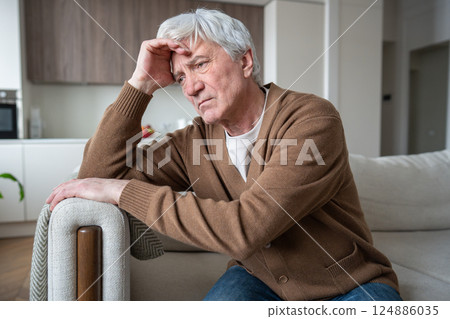 Lost sad elderly man with Alzheimer dementia sitting slumped on sofa, silent despair frustration 124886035