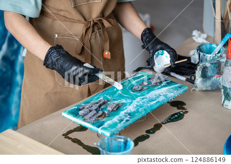 Artist hands in gloves shape waves in epoxy resin with wood spatula, add white pigment for sea foam 124886149