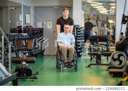 Motivated disabled man in wheelchair heading to workout session with supportive coach in gym Motivated disabled man in wheelchair heading to workout session with supportive coach in gym 124886221