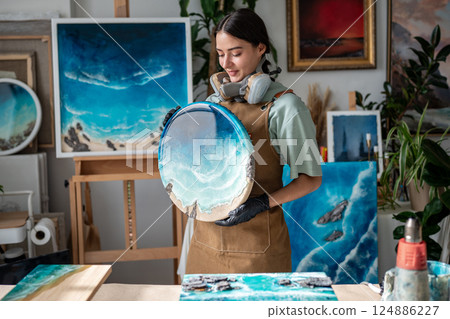 Content female artist in protective gear prepares round resin artwork with ocean waves in studio Content female artist in protective gear prepares round resin artwork with ocean waves in studio 124886227