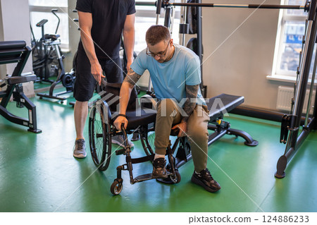 Professional sports trainer help disabled man in wheelchair move from exercise machine to wheelchair 124886233