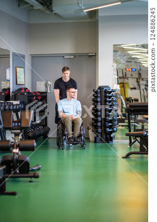Personal sports trainer pushing wheelchair athlete to gym for rehabilitation training after accident 124886245