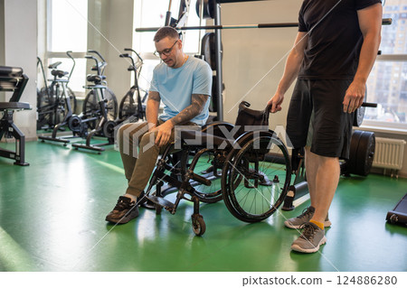Calm focused disabled man transfers from wheelchair to upper body strengthening machine in gym Calm focused disabled man transfers from wheelchair to upper body strengthening machine in gym 124886280
