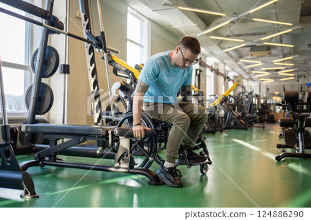Sportive disable man moves from wheelchair to upper body workout machine for exercising in gym Sportive disable man moves from wheelchair to upper body workout machine for exercising in gym 124886290