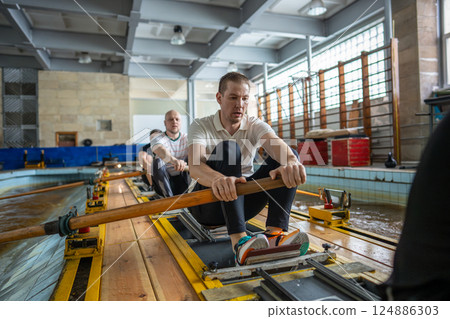Fatigued focused athletes train rigorously on rowing simulator in gym pool pushing past exhaustion 124886303