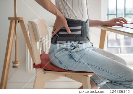 Man wearing back support belt on lower back during exacerbation to treatment of hernia. 124886345