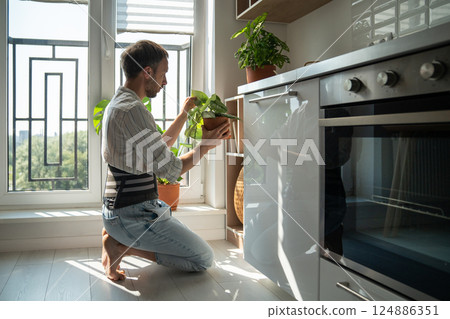 Young man wearing back support belt taking care of houseplants at home 124886351
