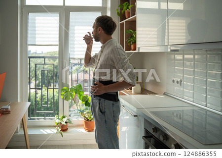 Young man wearing spinal brace drinking water recovering from back injury at home 124886355