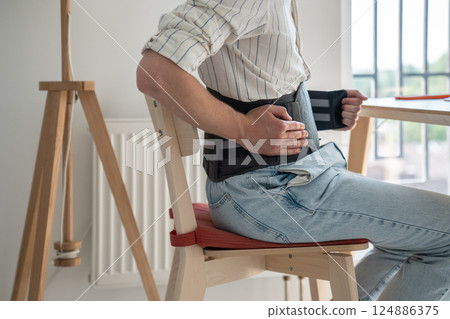 Man sitting at table wearing medical corset for lumbar spine Man sitting at table wearing medical corset for lumbar spine 124886375