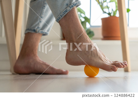 Man using silicone ball for foot massage during long sedentary work, legs close-up. 124886422