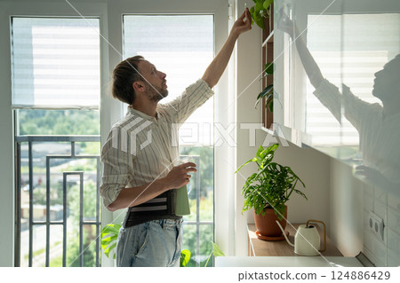Man in sick leave taking care houseplants at home on kitchen wearing back support belt corset. 124886429