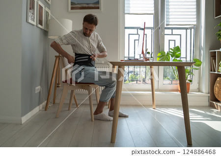 Man fixing belt corset before starting work to ease load on spine after an exacerbation hernia. Man fixing belt corset before starting work to ease load on spine after an exacerbation hernia. 124886468