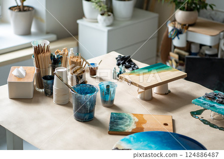 Epoxy art for water wave patterns. Table cluttered with brushes paints and board of drying artwork 124886487