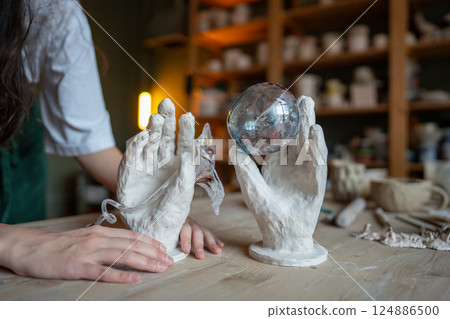 Creation of own production glass for sculpture in workshop. Glass ball in clay hands, handmade decor Creation of own production glass for sculpture in workshop. Glass ball in clay hands, handmade decor 124886500
