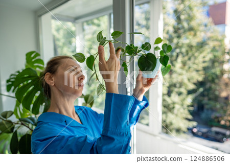 Enthusiastic middle aged woman inspects Philodendron leaves at home. Hobby for mental health. Enthusiastic middle aged woman inspects Philodendron leaves at home. Hobby for mental health. 124886506