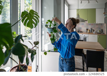 Enthusiastic middle aged woman inspects Philodendron leaves at home. Hobby for mental health. Enthusiastic middle aged woman inspects Philodendron leaves at home. Hobby for mental health. 124886525