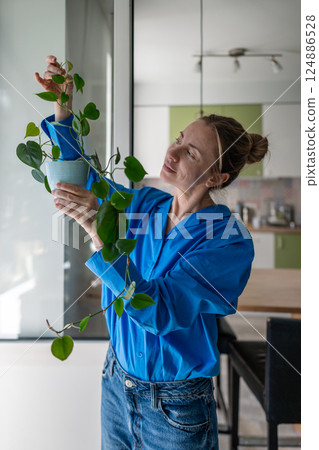 Enthusiastic middle aged woman inspects Philodendron leaves at home. Hobby for mental health. Enthusiastic middle aged woman inspects Philodendron leaves at home. Hobby for mental health. 124886528